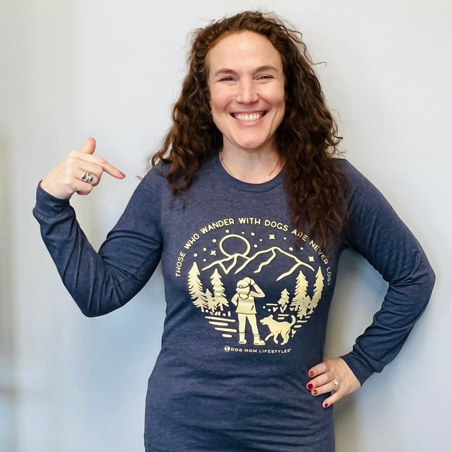 Person wearing a blue long-sleeve shirt with a graphic design, pointing to the shirt.